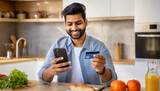 Happy Arabian man with phone and credit card using instant mobile payment at home kitchen Indian guy male customer shopper buyer buying online purchase smartphone shopping food delivery e-banking app