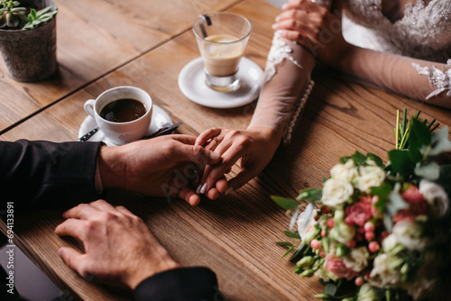 Young beautiful couple in love sitting in a cafe, hugging, touching each other with their hands. Wedding day, celebration, restaurant, coffee shop. The bride and groom drink coffee. photo