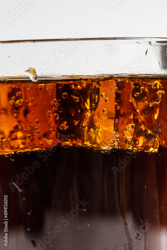 Carbonated drink with bubbles and ice in a glass on a white background, delicious drink