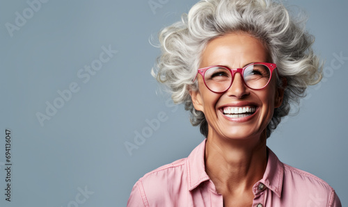 Confident and happy senior woman with stylish gray hair and glasses, smiling broadly, exuding positivity and experience on a light gray background