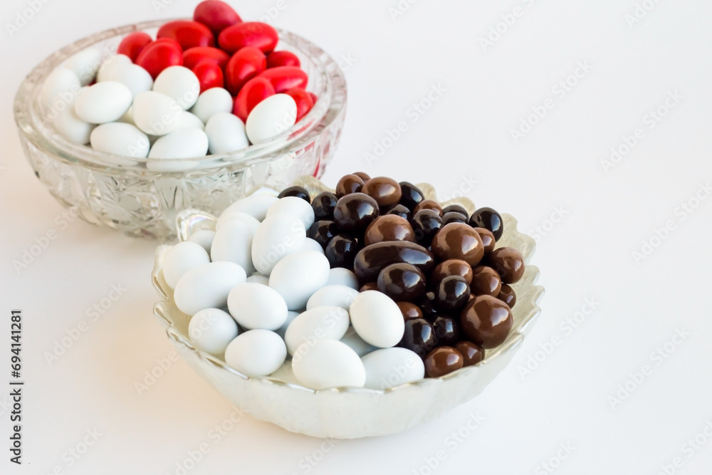 White and red color almond candies and dark chocolate balls designed half and half in the round candy bowl White and red color almond candies and dark chocolate balls designed half and half in the round candy bowl