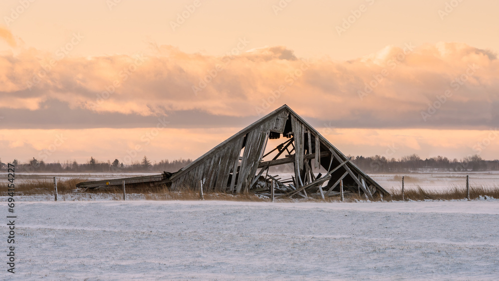 Old dilapidated barn in snowy field at dawn