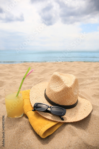 Straw hat  sunglasses  towel and refreshing drink on sandy beach near sea. Space for text