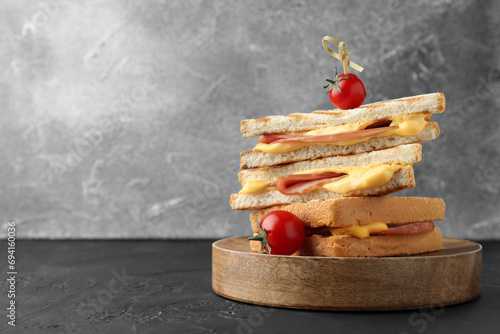 Fototapeta Naklejka Na Ścianę i Meble -  Stack of tasty sandwiches with ham and melted cheese served with tomatoes on black textured table, space for text