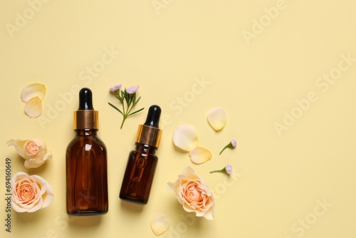 Bottles of cosmetic serum  beautiful flowers and petals on pale yellow background  flat lay. Space for text