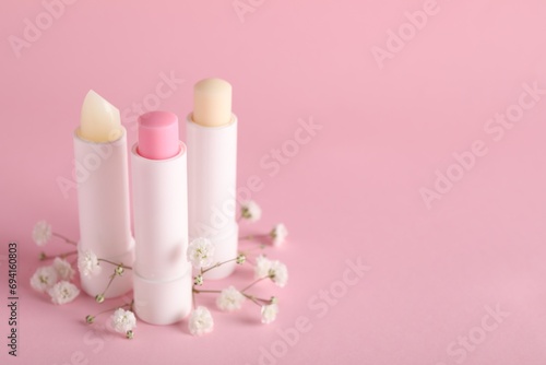 Different lip balms and gypsophila on pink background, space for text