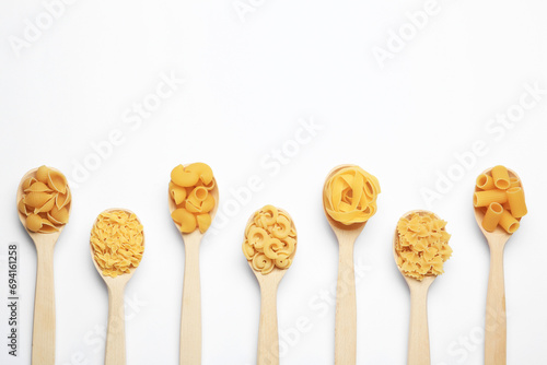 Different types of pasta in spoons on white background, flat lay. Space for text photo