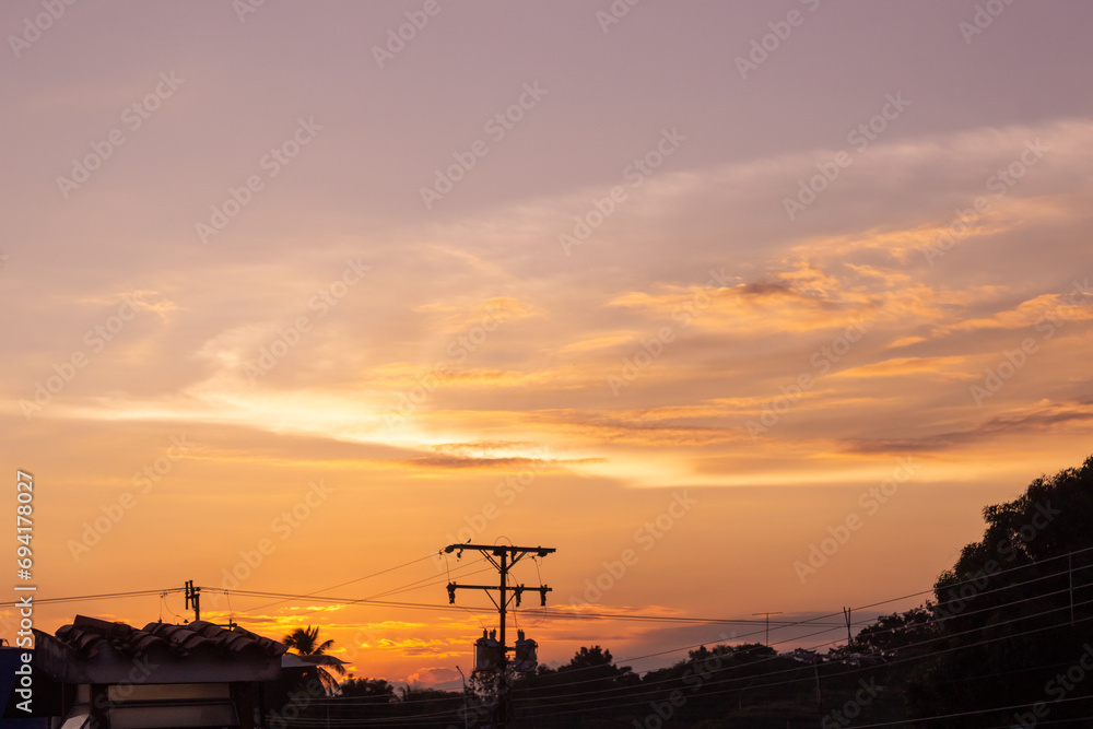 Naklejka premium Silhouette of electric pole at sunset with orange sky background.