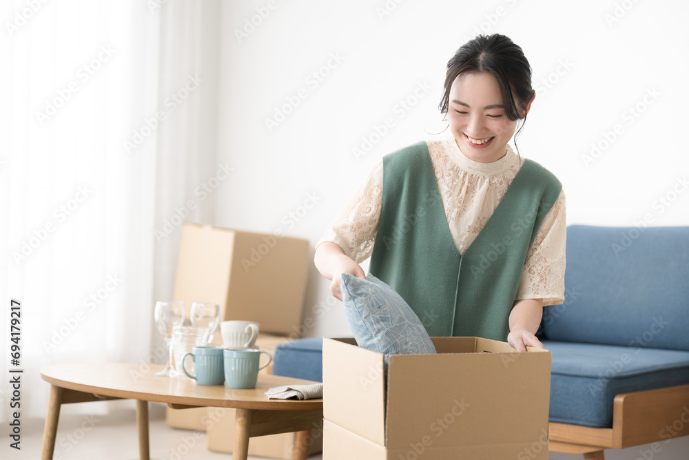 A smiling young woman packing cardboard boxes in preparation for a move. A smiling young woman packing cardboard boxes in preparation for a move.