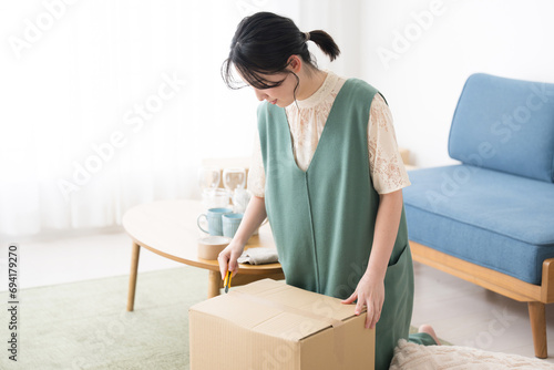 A young woman unpacking cardboard boxes with a cutter after the move. photo