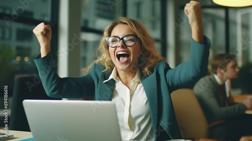 A young businesswoman in front of a laptop cheerfully celebrates success