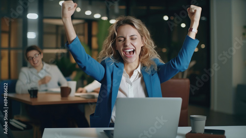 A young businesswoman in front of a laptop cheerfully celebrates success