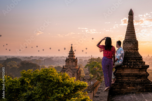 Bagan Myanmar  a couple of men and women are looking at the sunrise on top of an old pagoda temple. a couple on vacation in Myanmar Asia visit the historical site of Bagan with hot air balloons 