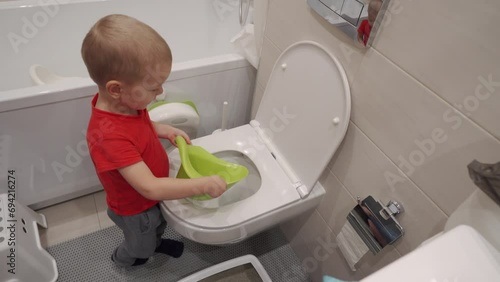Toddler child learns to pour the contents of potty down the toilet photo