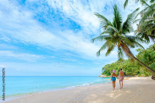 Fototapeta Naklejka Na Ścianę i Meble -  Phuket Thailand, a couple of men and woman walking at the beach of Surin, Surin Beach Phuket. A couple walking on a tropical beach with palm trees