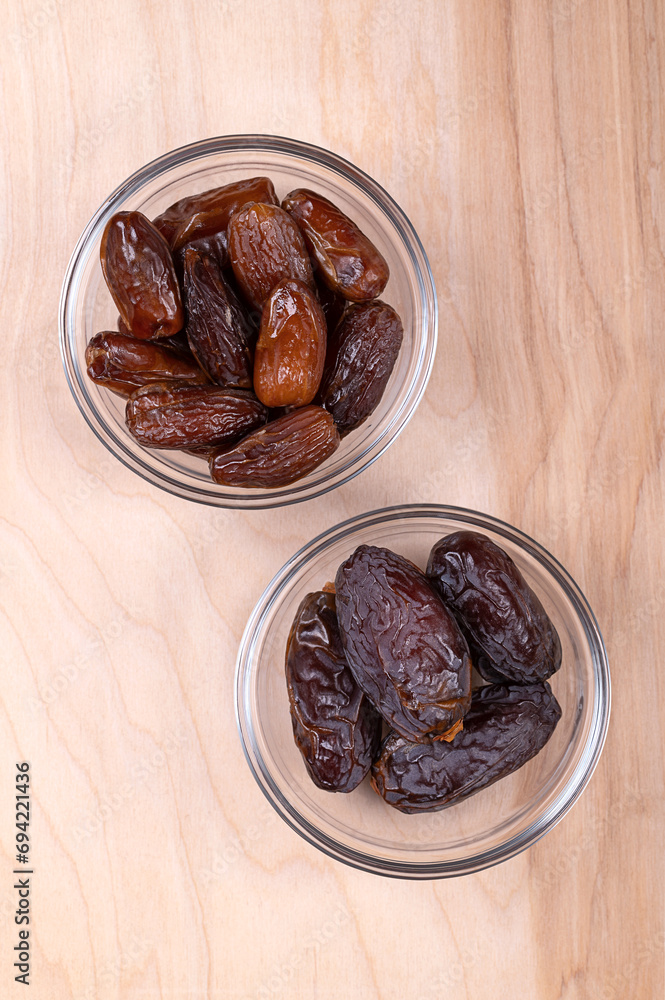 Deglet Nour and Medjool dates, in glass bowls, on a wooden panel, from