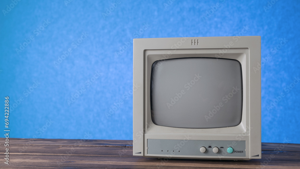 A gray antique TV on a wooden table on a blue background.