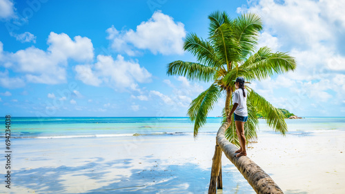 Young woman at a palm tree on a white tropical beach with turquoise colored ocean Anse Volbert beach Praslin Tropical Seychelles Islands. Cote D'or beach Praslin Seychelles photo
