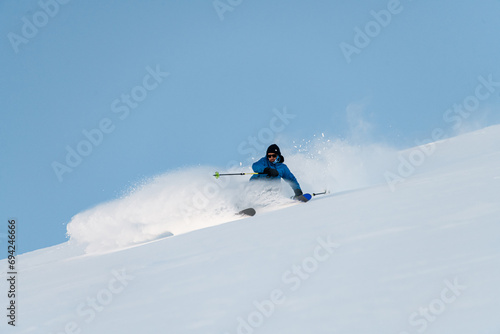 Skier in a blue ski suit goes down the slope with poles in his hands