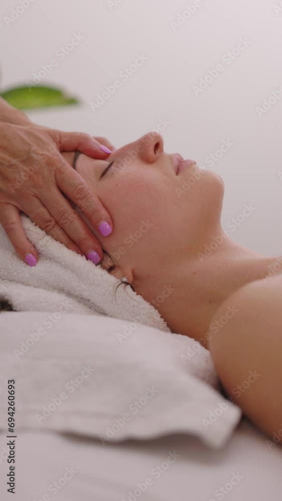 Therapeutic facial massage treatment for young beautiful woman in a medical massage salon. Massage therapist is doing stroking and pushing movements in this scene, side view. Vertical footage. Therapeutic facial massage treatment for young beautiful woman in a medical massage salon. Massage therapist is doing stroking and pushing movements in this scene, side view. Vertical footage.
