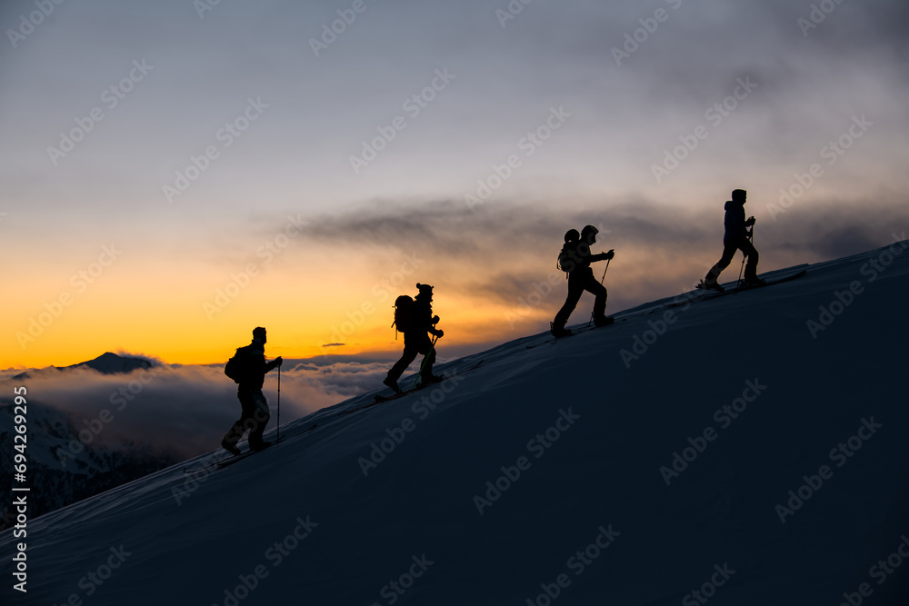 Close-up silhouettes of four skiers who reached the highest point of the mountain after sunset