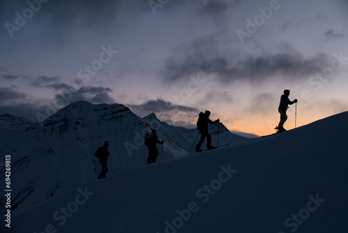 Silhouettes of four skiers on the highest point of the mountain massif after sunset