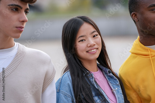 A young Asian woman smiles at the camera, flanked by her friends in a relaxed, outdoor setting, reflecting friendship and diversity