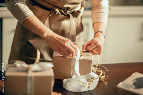Close up womans hands tie ribbon on box for customer order. Bakery chef baking pastry and cake in the kitchen. Small business entrepreneur and food delivery concept. © Айман Дайрабаева