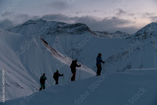 Silhouettes of four skiers climbing a mountain slope one after the other