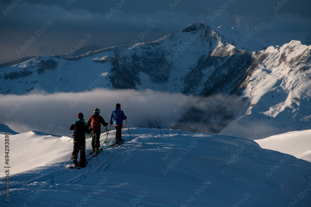 Three male skiers are walking one after the other on a snow-covered mountain peak
