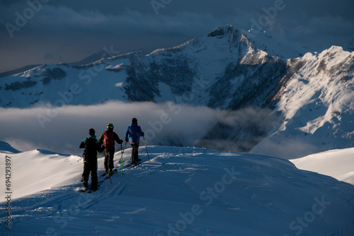 Three male skiers are walking one after the other on a snow-covered mountain peak