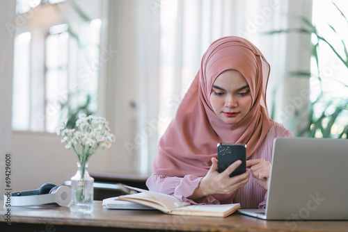 Beautiful young arab muslim business woman in a hijab working at her smartphone and computer at cafe.
