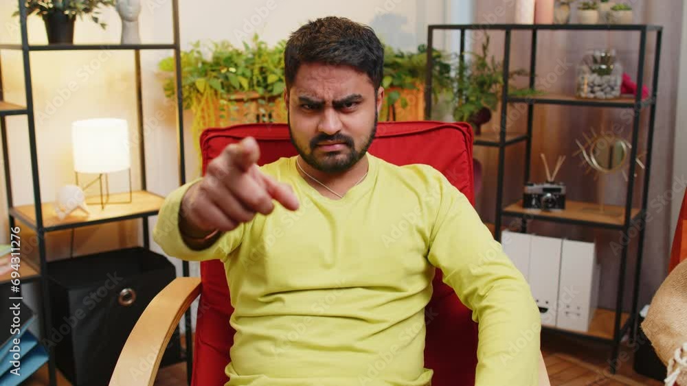 Hey you. Strict unhappy Indian man pointing hand finger to camera, looking angry, making choice, choosing guilty, noticing suspicious, accusing for mistake at home room apartment. Guy sits on chair Hey you. Strict unhappy Indian man pointing hand finger to camera, looking angry, making choice, choosing guilty, noticing suspicious, accusing for mistake at home room apartment. Guy sits on chair