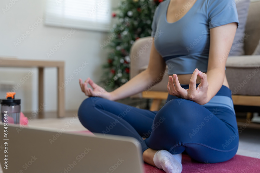 Young Asian woman meditating with trainer online on laptop at home