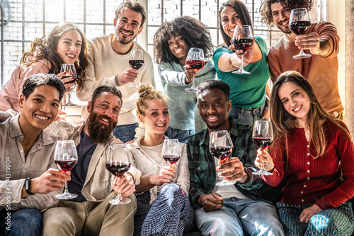 Group of friends toasting red wine sitting at living room at home - Gen z and millennial people enjoying party together - Lifestyle concept with guys and girls