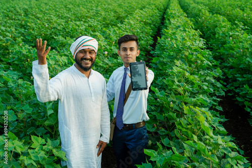 Young indian agronomist showing some information to farmer in tablet at agriculture field. photo
