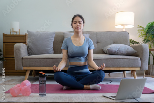 Young Asian woman meditating with trainer online on laptop at home