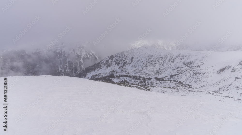 The white snowy peaks of Pirin covered with snow and fog. Snowy weather conditions for winter sports and tourism. Bansko Alpine Ski Resort, Bulgaria. The white snowy peaks of Pirin covered with snow and fog. Snowy weather conditions for winter sports and tourism. Bansko Alpine Ski Resort, Bulgaria.