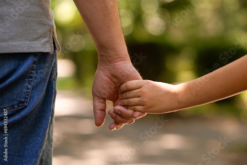 the father's hand held tightly the hand of his little son against the background of green foliage, close-up