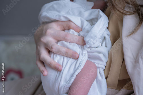 A mother's hand gently hugs a newborn baby.