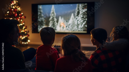 Family watching a Christmas movie together in a cozy living room decorated with a lit Christmas tree during the holiday season.