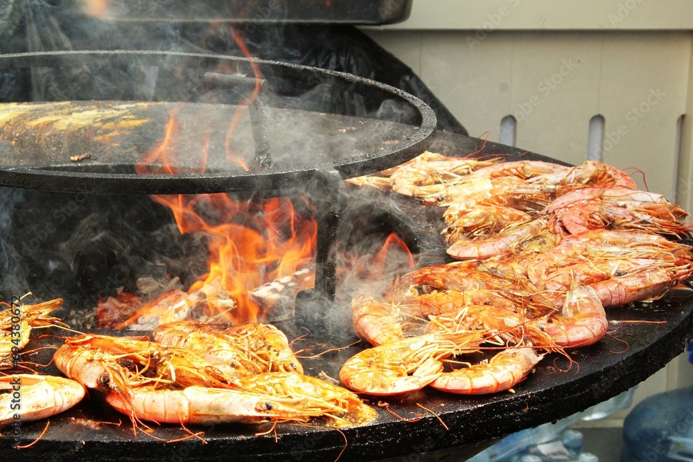 Seafood slices are cooked on a fire pit surface in the shape of cone shaped bowl. Bowl-shaped flat grill with prawns and shrimps. Outdoor barbecue cooking. Street food concept. Toast the hot grilled