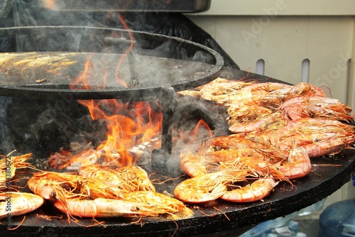 Seafood slices are cooked on a fire pit surface in the shape of cone shaped bowl. Bowl-shaped flat grill with prawns and shrimps. Outdoor barbecue cooking. Street food concept. Toast the hot grilled