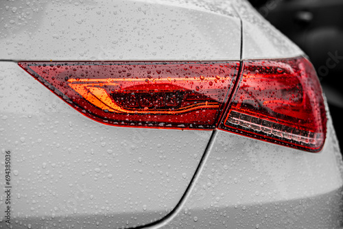 Close-up of the rear lights of a luxurious white Mercedes car with raindrops all over it