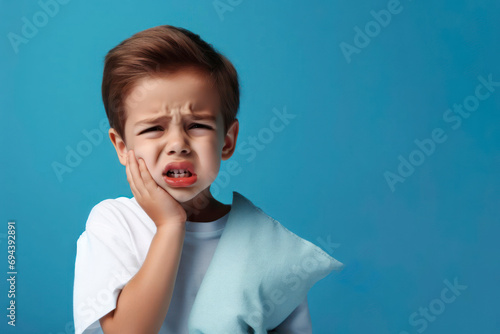 kid suffering from toothache holding his chin with his hand on blue background. ai generative photo