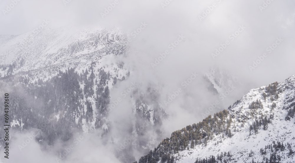 Obraz premium The white snowy peaks of Pirin covered with snow and fog. Snowy weather conditions for winter sports and tourism. Bansko Alpine Ski Resort, Bulgaria.