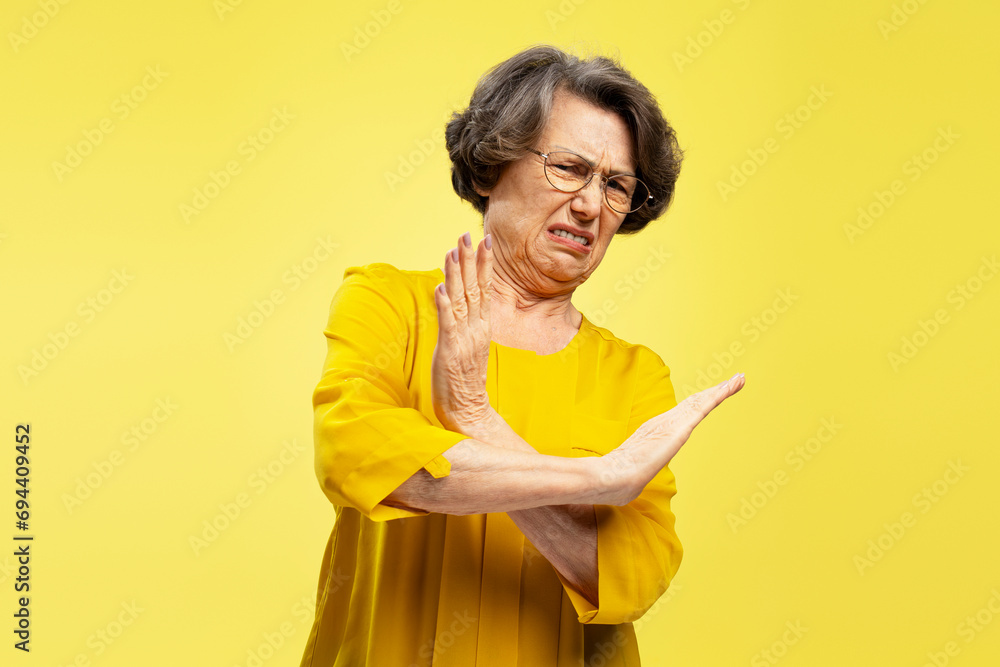 Portrait of unhappy, gray haired woman showing hands stop gesture isolated on yellow background Portrait of unhappy, gray haired woman showing hands stop gesture isolated on yellow background