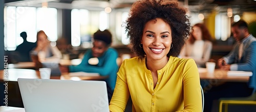 Cheery mixed-race woman in yellow shirt happily trains and takes notes with students to be executives at a laptop table.