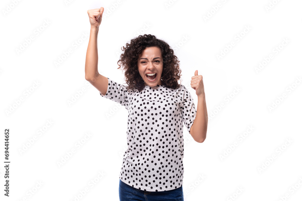 young stylish woman with curly hair dressed in a blouse with polka dots smiles and feels happy