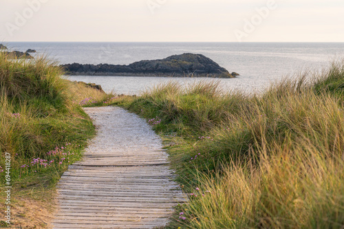 A path, leading through grassy sand dunes overlooking the ocean. it is evening and the scene is bathed in golden light photo